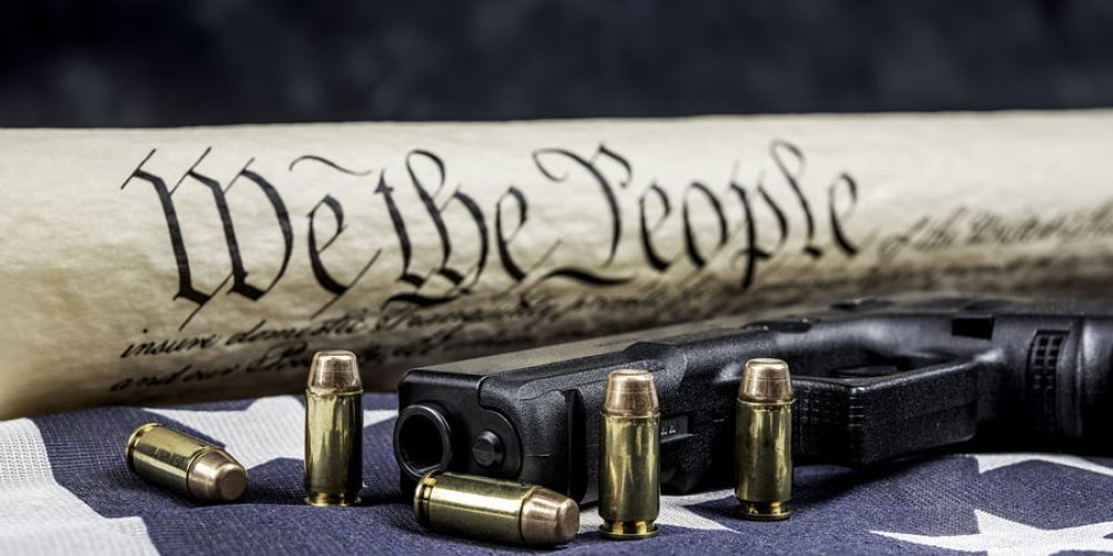 A handgun with bullets symbolizing gun rights while framed against the United States constitution.
