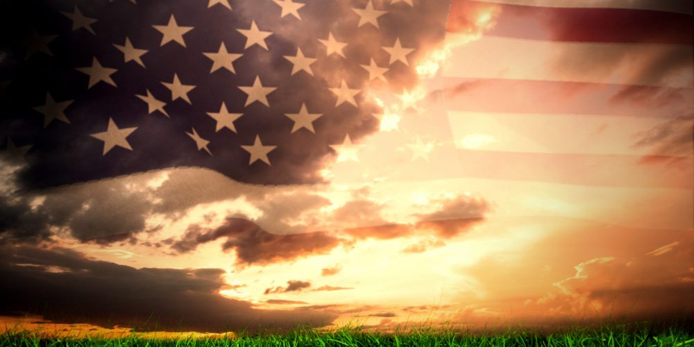 United states of america flag against green grass under blue and orange sky